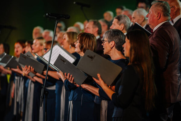 Валмиера, Латвия - 8 февраля 2025 - вечеринка 90-х годов. Хор поет на сцене, держа в руках песенники в синхронном исполнении, одетый в формальный наряд при освещении сцены..