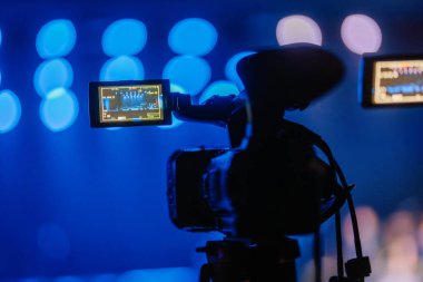 Valmiera, Letonya - 29 Aralık 2024 - Profesyonel bir video kamera, LCD ekranı sahneyi gösteren bir olayı kaydeder. Bulanık mavi sahne ışıkları dramatik bir konser ortamı yaratır..