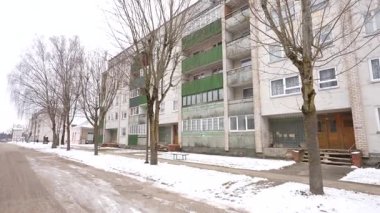 Seda, Letonya - 12 Şubat 2025 - Yeşil balkonları ve yıpranmış cephesi olan eski Sovyet döneminden kalma apartman dairesi, karlı bir kış gününde caddede yapraksız ağaçlarla kaplanmış..