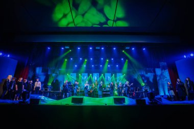 Valmiera, Letonya - 29 Aralık 2024 - Yamaha etkinliği. Büyük bir koro ve bando canlı bir konser sırasında canlı mavi ve yeşil ışıklı, dijital ekranlı ve dinamik atmosferli bir sahnede performans sergiliyor..