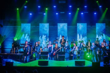 Valmiera, Letonya - 29 Aralık 2024 - Yamaha etkinliği. Büyük bir grup şarkıcı ve müzisyen renkli ışıklandırma, dijital ekranlar ve enstrümanlarla sahnede performans sergileyerek dinamik bir konser ortamı yarattılar..