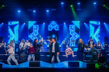 Valmiera, Letonya - 29 Aralık 2024 - Bir Yamaha etkinliğinde canlı canlı performans, canlı mavi LED görselleri ve dramatik ışıklandırması olan şarkıcılar, müzisyenler ve dansçıların sahne aldığı.