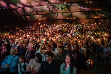 Valmiera, Latvia - December 29, 2024 - A large audience in a concert hall holds up lights and smartphones, creating a warm, festive atmosphere at a Yamaha event. People are engaged and enjoying the moment. clipart