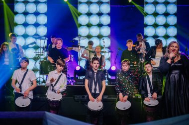 Valmiera, Letonya - 29 Aralık 2024 - Bir grup genç vurmalı çalgıcı, bateristler, gitaristler ve bir Yamaha etkinliğinde canlı ışıklandırma efektleriyle birlikte sahnede djembes çalıyorlar..