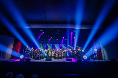 Valmiera, Letonya - 29 Aralık 2024 - Yamaha 'da, renkli ışıklar ve dinamik efektlerin yer aldığı parlak bir sahnede şarkıcılar, müzisyenler ve davulcularla birlikte büyük bir canlı performans.