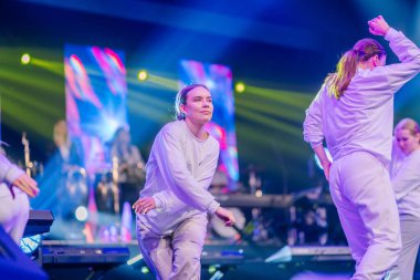 Valmiera, Letonya - 29 Aralık 2024 - Bir grup dansçı Yamaha etkinliğinde sahnede canlı ışıklandırılmış beyaz elbiseler ve sahneyi renklendiren renkli dijital arka plan ile performans sergiliyorlar..