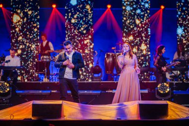 Valmiera, Letonya - 29 Aralık 2024 - Bir erkek ve kadın şarkıcı, yıldızlı dijital fon, müzisyenler ve atmosferik ışıklandırma ile bir Yamaha etkinliğinde düet yaptılar.