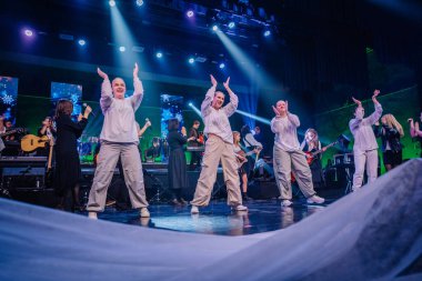 Valmiera, Letonya - 29 Aralık 2024 - Bir Yamaha etkinliğinde enerjik dansçılar canlı ışıklandırma ve şenlikli bir fon altında müzisyen ve şarkıcılarla senkronize olarak sahnede performans sergiliyorlar..