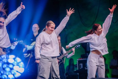 Valmiera, Letonya - 29 Aralık 2024 - Yamaha 'daki bir etkinlikte sahne alan enerjik dansçılar, arka planda müzik aletleri çalan müzisyenler ve beyaz kıyafetler giydiler..