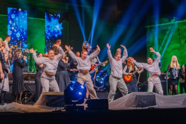 Valmiera, Letonya - 29 Aralık 2024 - Bir Yamaha etkinliğinde canlı yeşil ve mavi sahne ışıklandırması altında müzisyen ve şarkıcıların eşlik ettiği enerjik dansçılar sahne alacaklar.