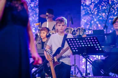 Valmiera, Letonya - 29 Aralık 2024 - Genç gitarist, müzisyenler, klavyeler ve bateristlerle çevrili bir Yamaha etkinliğinde sahne aldı. Canlı sahne ışıklandırması konser atmosferini güçlendirir.