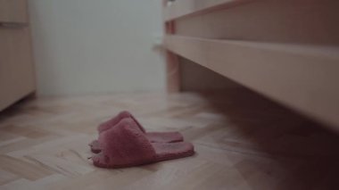 Çıplak ayakla, ahşap bir zeminde, yumuşak pembe terliklere basan, rahat ve rahatlatıcı bir sabah anını yakalayan bir insan..