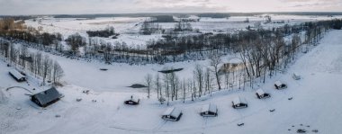 Yapraksız ağaçlarla çevrili karlı bir nehir kenarı yerleşim yeri ve kışın donmuş bir nehir manzarası..