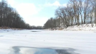 Karla kaplı bir arazi ve çıplak ağaçlarla çevrili donmuş bir nehrin hava görüntüsü, bir kış insansız hava aracı uçuşu sırasında çekildi..