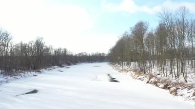 Karla kaplı bir arazi ve çıplak ağaçlarla çevrili donmuş bir nehrin hava görüntüsü, bir kış insansız hava aracı uçuşu sırasında çekildi..