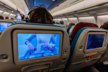 Riga, Letonya - 22 Şubat 2025 - Uçak yolcuları uçuş sırasında güvenlik videosu izliyorlar. Kabin yukarıdaki ışıklarla aydınlatılıyor ve rahat bir yolculuk ortamı yaratıyor..