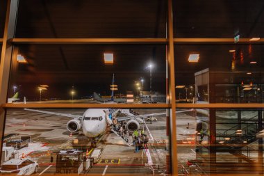 Riga, Letonya - 22 Şubat 2025 - Yolcular havaalanı penceresinden görülen bir merdivenden gece Ryanair uçağına binerler. Pist, zemin araçları ve terminal yansımaları derinlik ekler.