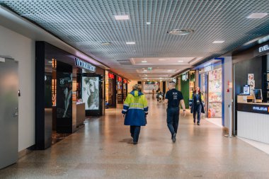 Riga, Letonya, 22 Şubat 2025 havaalanı güvenlik görevlileri havaalanı terminalinde devriye geziyor. Arka planda Victoria Sırrı da dahil olmak üzere lüks mağazalar görülüyor.