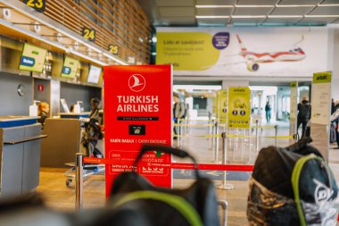 Riga, Letonya - 22 Şubat 2025 - Türk Hava Yolları, bagaj levhası ve gişeleri olan bir havaalanında kayıt yaptırıyor. AirBaltic marka ve arka planda yolcular.