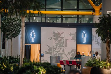 Istanbul, Turkey - February 23, 2025 - A modern public restroom entrance with illuminated male and female symbols, wooden doors, and decorative walls in an airport setting. clipart