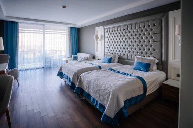 Serik, Türkiye - 22 Şubat 2025 - İki yataklı, lüks yatak başlıklı ve balkonlu şık bir otel odası. Mavi aksanlı parlak ve modern iç mekan.