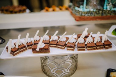 Krem şanti ve beyaz çikolata süslemeleriyle kaplı bir tabak zarif çikolatalı kek, tatlı büfesinde sergileniyor..