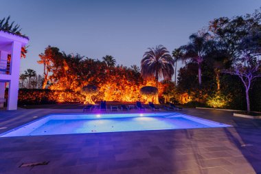 Endülüs, İspanya, 30 Ocak 2025 - Tropikal bir ortamda sıcak çevre ışıklandırması ve palmiye ağaçları ve yemyeşil ile çevrili, gece aydınlatılmış lüks bir açık havuz.