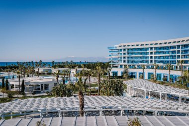 Serik, Türkiye - 24 Şubat 2025 - Modern mimarisi, palmiye ağaçları, yüzme havuzları ve açık mavi gökyüzünün altında bir dağ manzaralı lüks bir sahil beldesi.