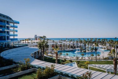 Serik, Türkiye - 24 Şubat 2025 - Palmiye ağaçları, havuzları, modern mimarisi ve açık mavi gökyüzü altında su kaydırakları olan lüks bir sahil beldesi.