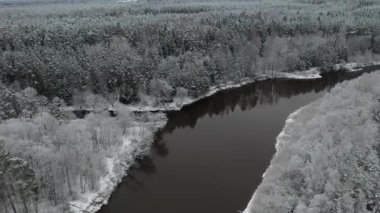 Karla kaplı bir orman ve uzak bir şehir manzarasıyla çevrili dolambaçlı bir nehrin üzerinde insansız hava aracı uçuşu nefes kesici bir kış manzarası yakalıyor..