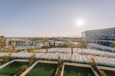 Serik, Türkiye - 24 Şubat 2025 - Sahil manzaralı, bereketli palmiye ağaçları, yüzme havuzları ve parlak güneşli gökyüzü altında modern mimarisi olan lüks bir tatil yeri.