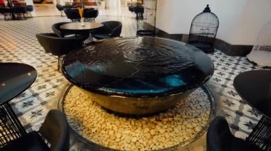 Modern bir siyah su çeşmesi şık bir kapalı salon salonunda desenli fayanslar, zarif siyah sandalyeler ve arka planda dekoratif kuş kafesleri ile..