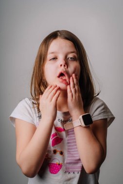 A young girl in a casual outfit makes a funny, exaggerated facial expression, pulling her mouth with her hands. She wears a smartwatch on her wrist. clipart