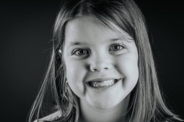 Siyah-beyaz, gülümseyen, dişleri dökülmüş, koyu bir arka planda mutlu ve anlamlı görünen genç bir kızın yakın plan portresi..