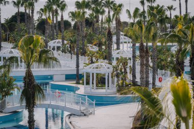 Palmiye ağaçları, beyaz çardaklar, köprüler ve dolambaçlı havuzu olan lüks bir tropikal tatil köyü deniz kenarında huzurlu bir tatil ortamı yaratıyor..