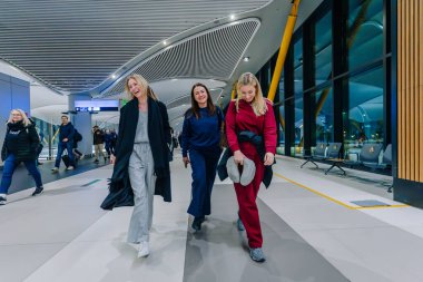 İstanbul, Türkiye - 22 Şubat 2025 Modern bir havaalanı terminalinde yürüyen, rahat seyahat kıyafetleri giymiş, gülümseyen ve yolculuklarının tadını çıkaran üç mutlu kadın.