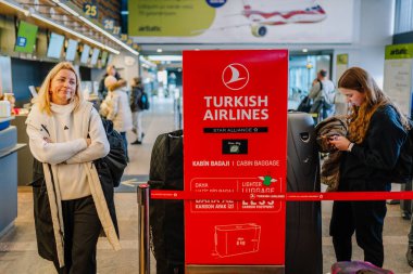 Riga, Letonya - 22 Şubat 2025 - Türk Hava Yolları kayıt alanındaki yolcular, havaalanındaki kırmızı bagaj politikası tabelasının yanında duruyor, arka planda yoğun bir terminal bulunuyor..