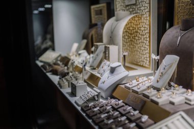 Serik, Türkiye - 1 Mart 2025 - Altın ve gümüş yüzükler, kolyeler, bilezikler ve yumuşak ışıklandırma altında zarif bir şekilde düzenlenmiş küpelerin yer aldığı lüks bir mücevher mağazası.