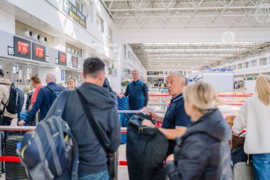 Antalya, Türkiye - 1 Mart 2025 - Havaalanı gişesinde bavulla bekleyen yolcular. Havaalanının yüksek tavanı ve parlak ışıklandırması olan modern bir tasarımı var..