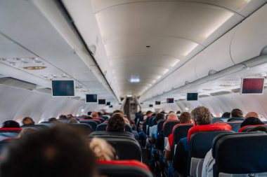 Antalya, Türkiye - 1 Mart 2025 - Bir uçuş sırasında oturan yolcularla dolu bir uçak kabininin iç görünümü. Üst bölmeler, ekranlar ve ışıklandırma görünür..