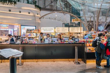 İstanbul, Türkiye - 01 Mart 2025 - Sipariş hazırlayan personeli ve yiyecek ve içecek satın alan yolcuları olan modern bir havaalanı kafesi. İç mekan şık bir dekor ve canlı bir atmosfere sahip..