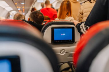 Riga, Letonya - 01 Mart 2025 - Türk Hava Yolları logosunu gösteren bir uçuş içi eğlence ekranı olan bir uçağın içindeki yolcular. Bazı yolcular otururken, diğerleri ayakta.