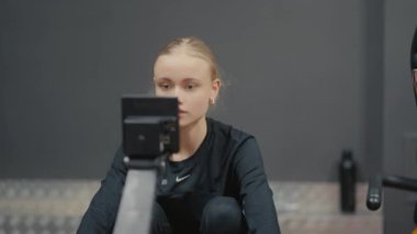 Valmiera, Letonya - 4 Şubat 2025 - Siyah spor kıyafetli genç bir kadın spor salonunda kürek çekme makinesinde egzersiz yapıyor, antrenmanına odaklanıyor. Arka planda bir su şişesi görünür..