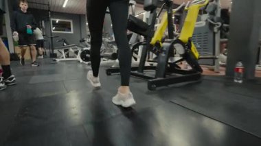Valmiera, Letonya - 4 Şubat 2025 - Bir kişi arka planda koşu bantları ve kürek makineleri de dahil olmak üzere spor salonunda spor aletleriyle yürür. Diğer insanlar spor yapıyor..