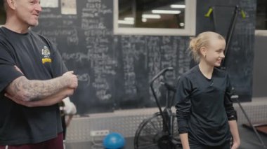 Valmiera, Letonya - 4 Şubat 2025 - Spor salonundaki genç bir kadın spor salonundaki antrenörüyle konuşur, spor aletleri ve spor notlarıyla çevrili bir karatahta.