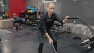 Valmiera, Letonya - 4 Şubat 2025 - odaklanmış bir kadın spor salonunda savaş halatlarıyla egzersiz yapar, dayanıklılık ve dayanıklılık sağlar. Arka planda çalışan başka biri daha var..