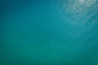 Uçsuz bucaksız, turkuaz bir okyanusun havadan görünüşü hafif dalgalanmalar ve su yüzeyinde titreyen yansımalarla sakin ve huzurlu bir manzara yaratıyor.