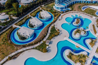 Serik, Türkiye - 28 Şubat 2025 - Lagün tarzı havuzlar, yemyeşil alanlar ve rahatlama için modern mimari ile çevrili özel villaları olan lüks bir tatil köyünün havadan görünüşü.