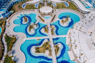 Serik, Türkiye - 28 Şubat 2025 - Benzersiz eğimli tasarımlar, köprüler ve palmiye ağaçları ile lüks bir tatil havuzu havuzu havuzu manzarası, tropikal bir tatil atmosferi yaratıyor.