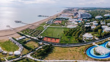 Serik, Türkiye - 28 Şubat 2025 - Sakin denize uzanan villaları, spor sahaları, havuzları, kabinleri ve ahşap iskeleleri olan lüks bir sahil beldesinin havadan görünüşü.